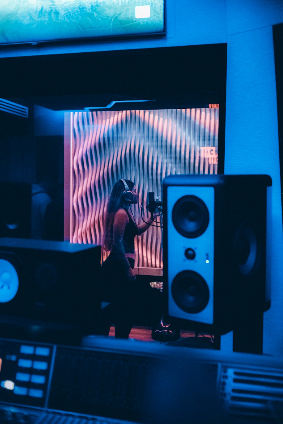 Woman with headphones singing into microphone in recording studio.