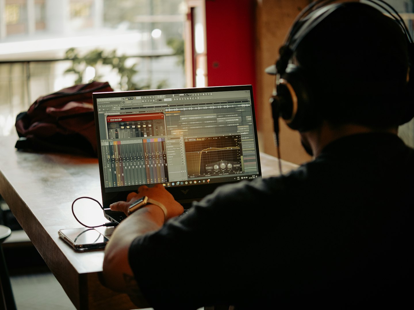 Person with headphones works on music production software at a table.