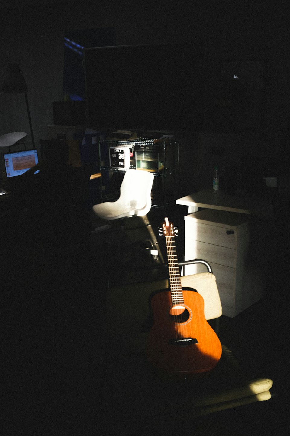 Acoustic guitar leaning against a chair in sunlight.